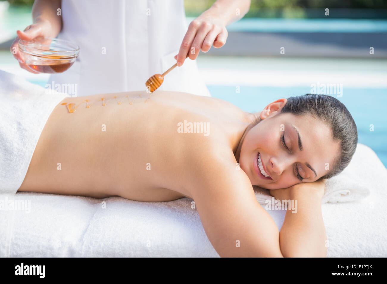 Happy brunette getting a honey beauty treatment poolside Stock Photo