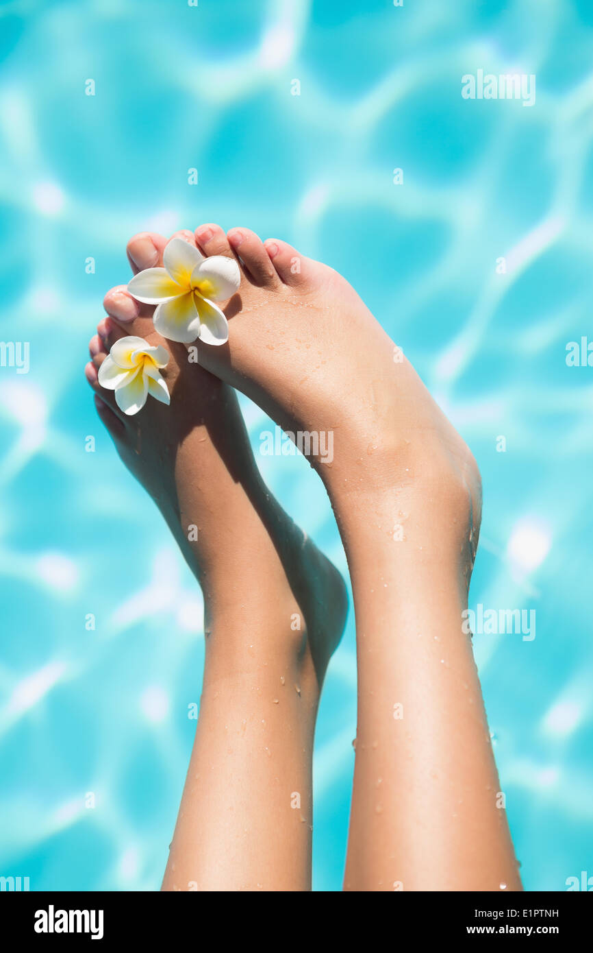 Feet dangling over swimming pool with flowers Stock Photo