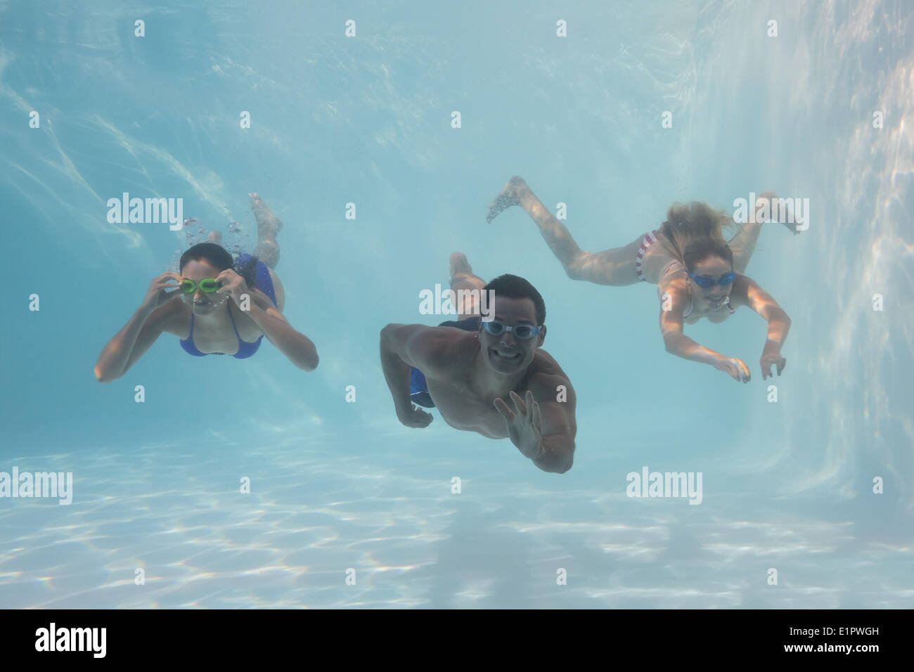 Smiling friends looking at camera underwater in swimming pool Stock Photo