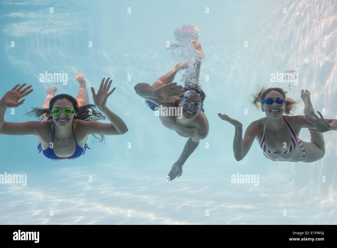 Smiling friends looking at camera underwater in swimming pool Stock Photo