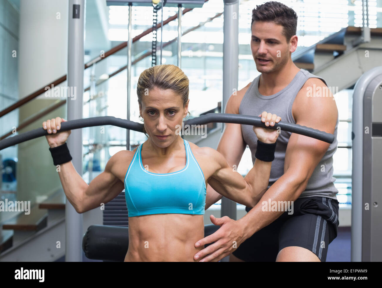 Female bodybuilder using weight machine for arms with encouraging