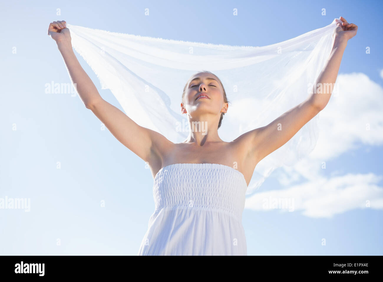 Pretty blonde in white dress holding up shawl on the beach Stock Photo