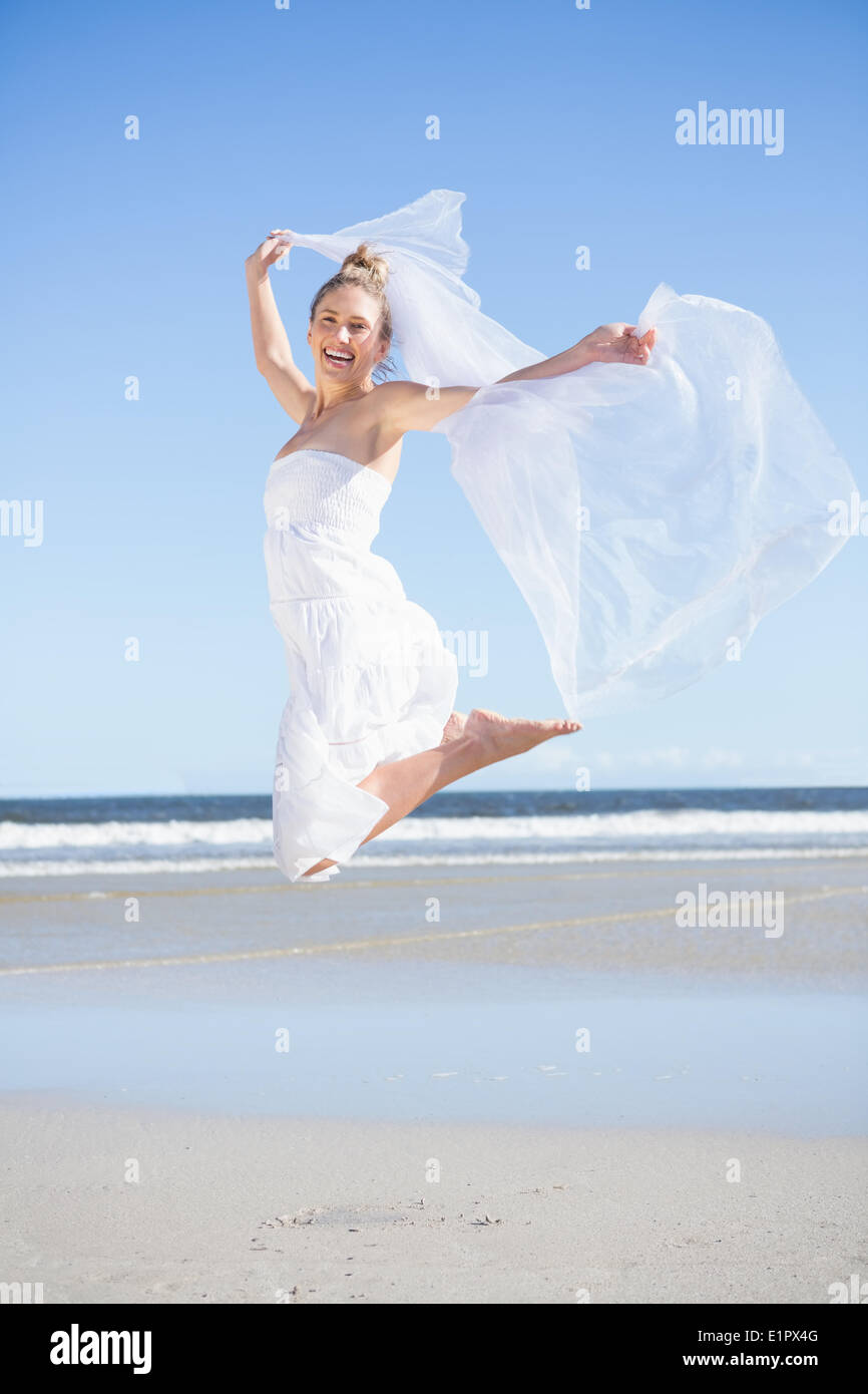 Pretty blonde in white dress holding up shawl on the beach Stock Photo