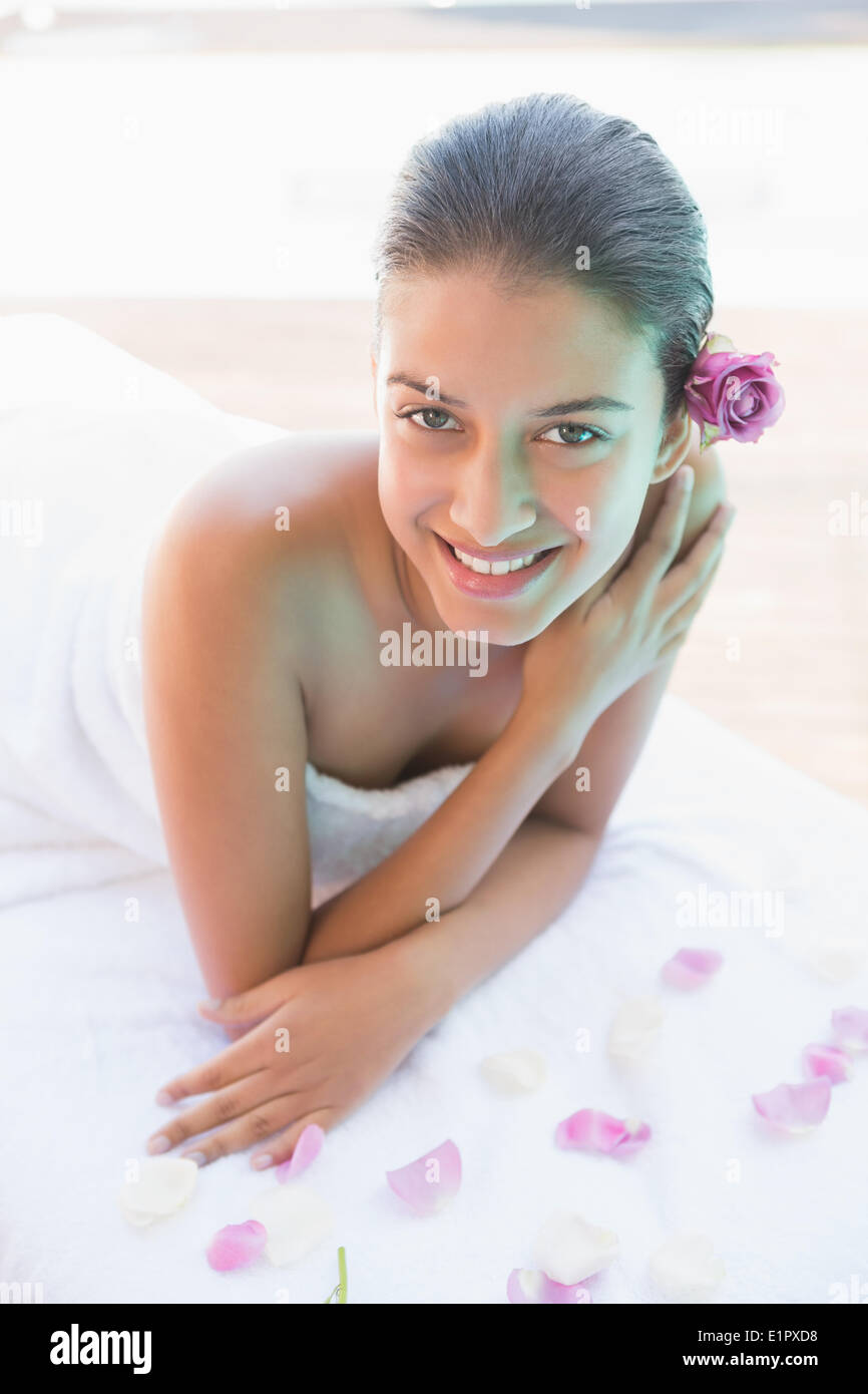 Smiling brunette lying on towel with rose petals Stock Photo