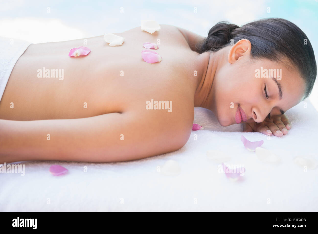 Smiling brunette lying on towel with rose petals Stock Photo