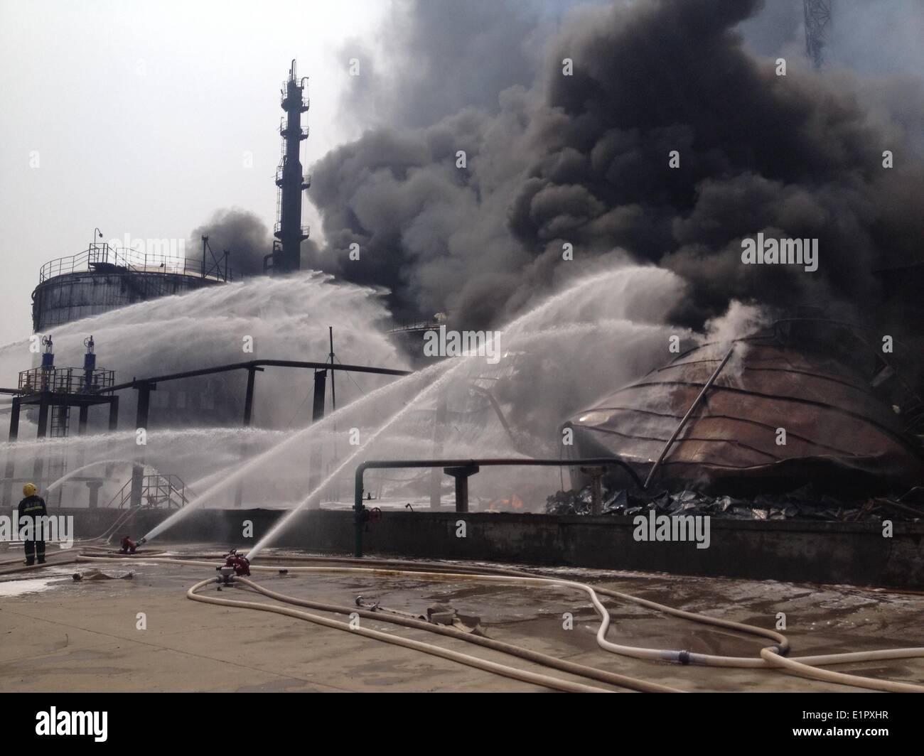 Nanjing, China's Jiangsu Province. 9th June, 2014. Photo taken with a mobile phone shows a fireman putting out fire at the accident site after an explosion ripped through the refinery of Sinopec Yangzi Petrochemical Co. in Nanjing, capital of east China's Jiangsu Province, June 9, 2014. Crude oil tanks near the sulfur recovery facility at the refinery exploded Monday noon, and three of eight oil tanks at the site were on fire after the explosion toppled them down. It was not immediately known whether the blast and fire have caused casualties. Credit:  Wang Wei/Xinhua/Alamy Live News Stock Photo