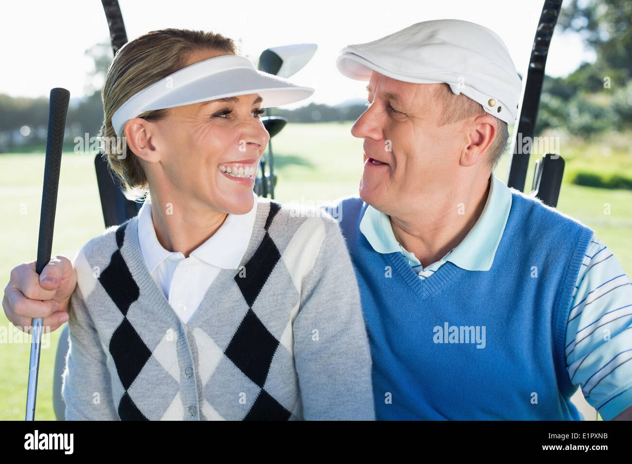 Happy golfing couple sitting in golf buggy smiling at each other Stock Photo