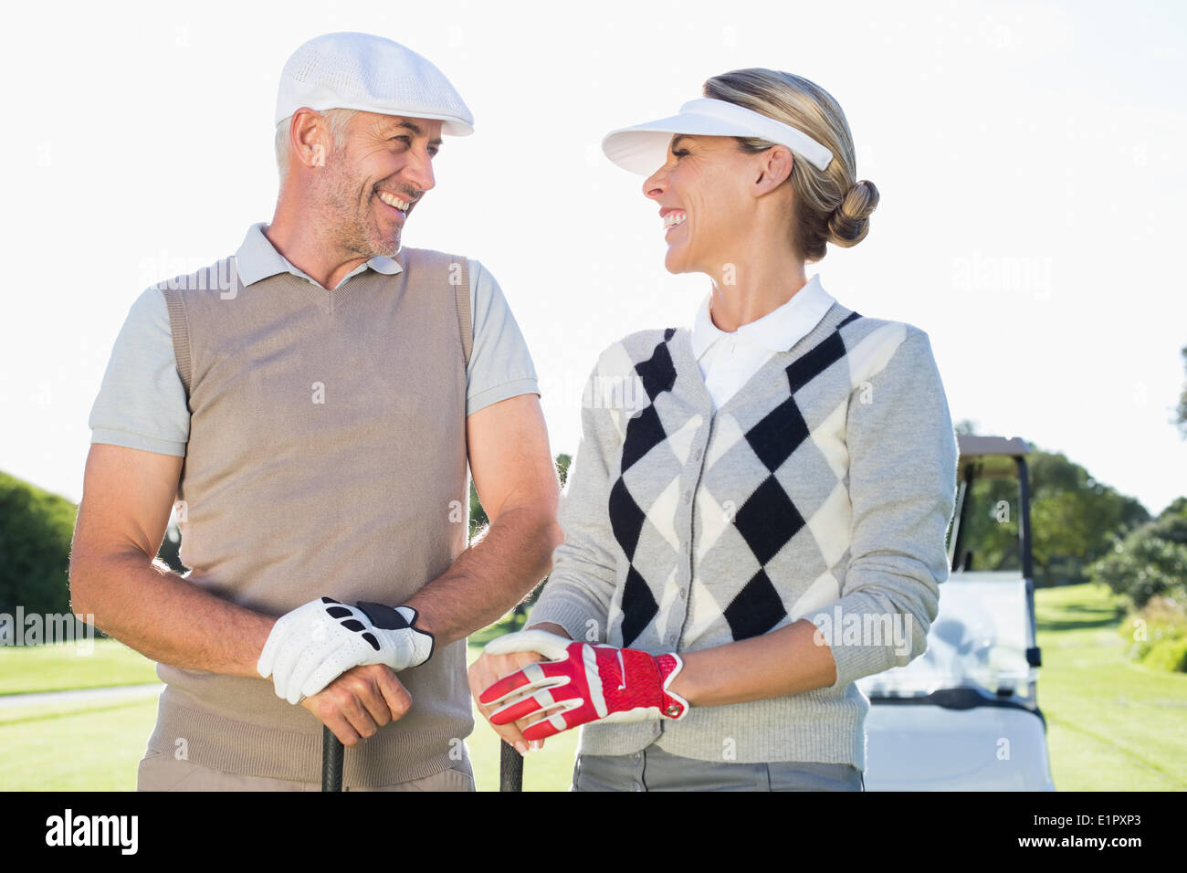 Happy golfing couple facing each other with golf buggy behind Stock Photo