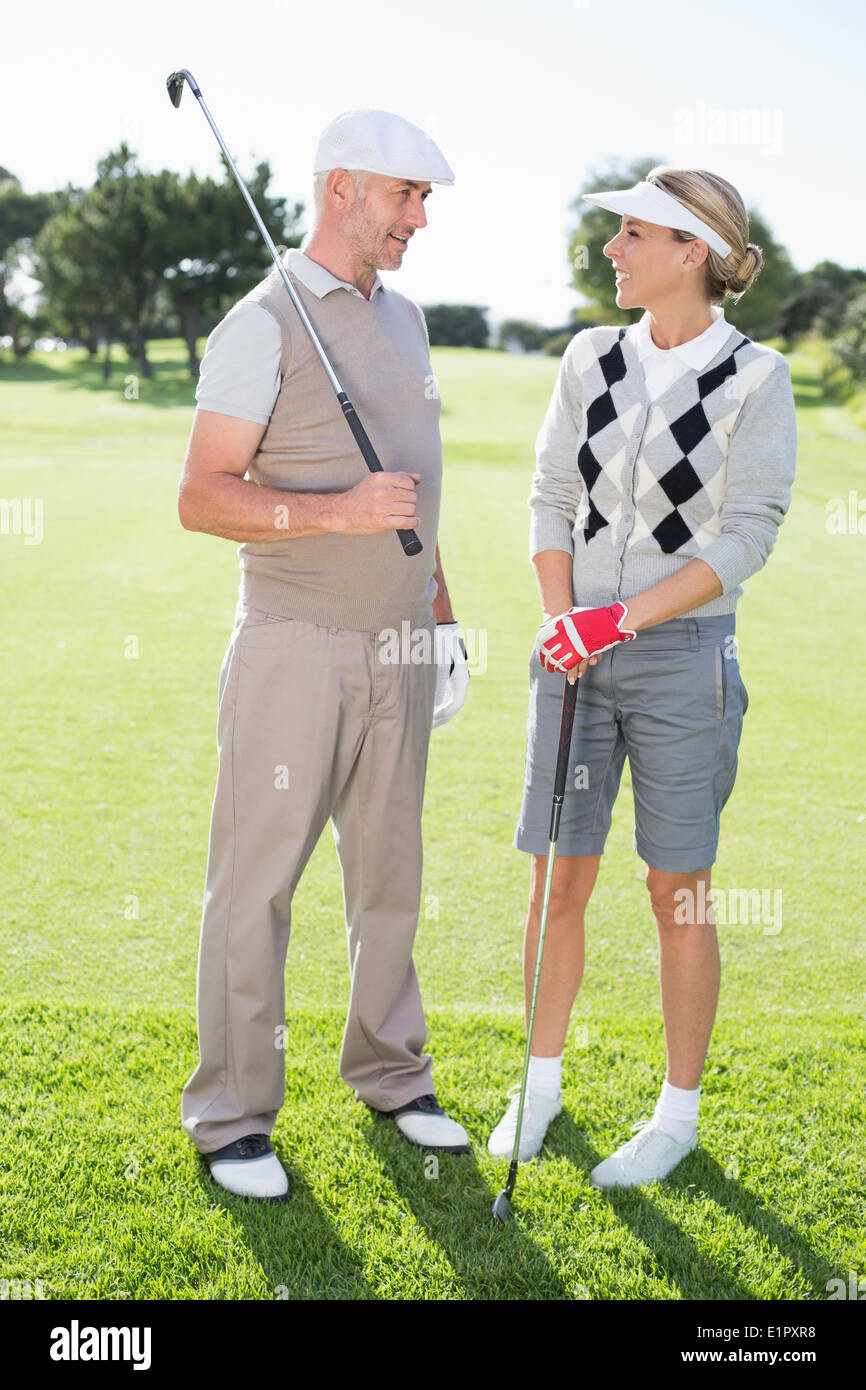 Golfing couple smiling at each other holding clubs Stock Photo