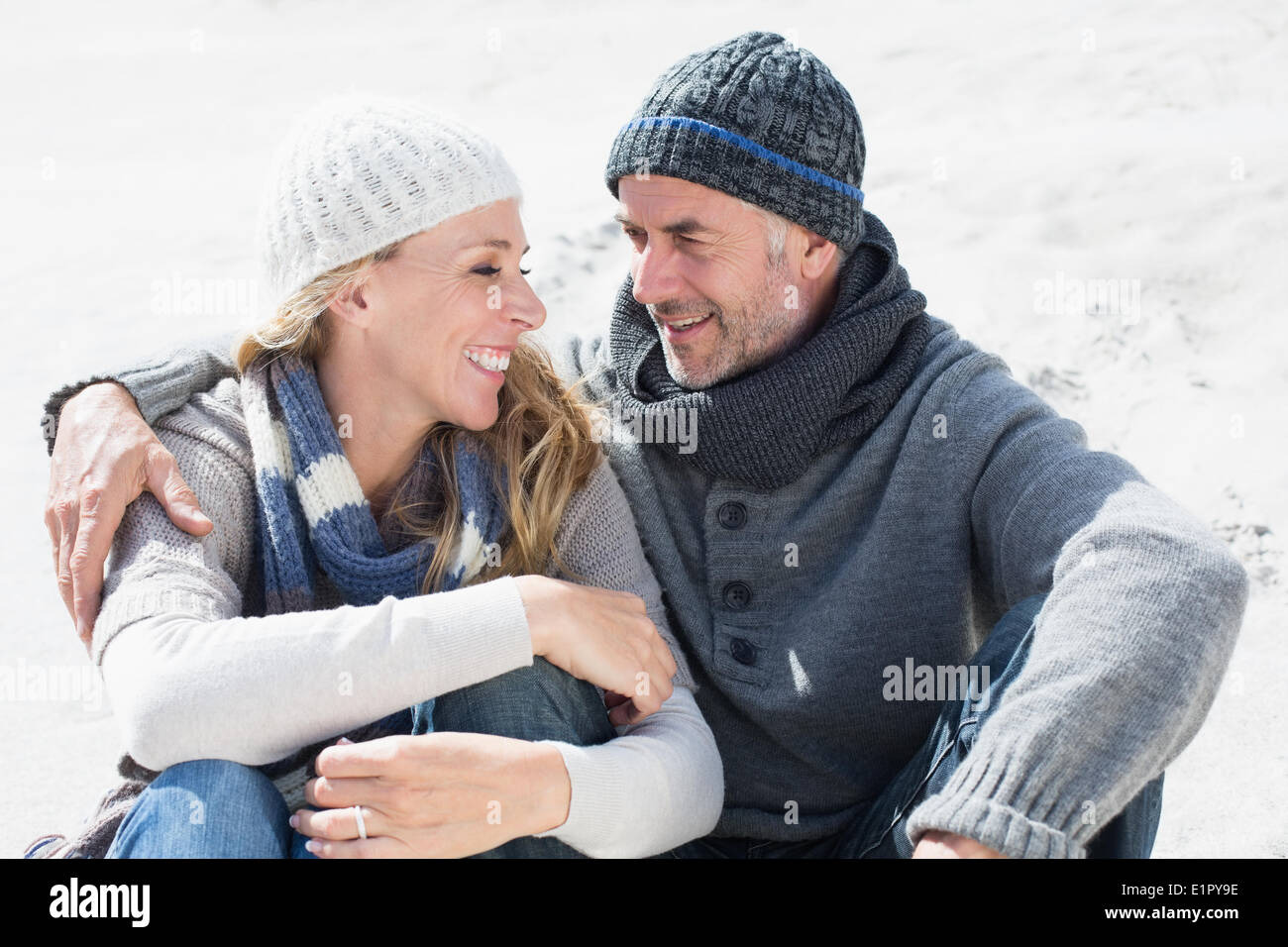 Attractive couple smiling at each other on the beach in warm clothing Stock Photo