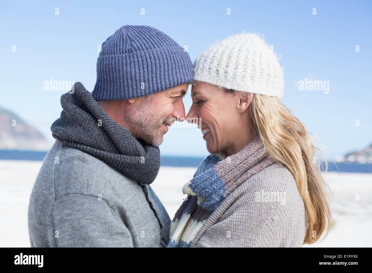 Attractive couple smiling at each other on the beach in warm clothing Stock Photo