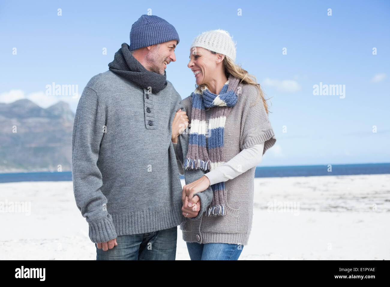 Smiling couple standing on the beach in warm clothing Stock Photo