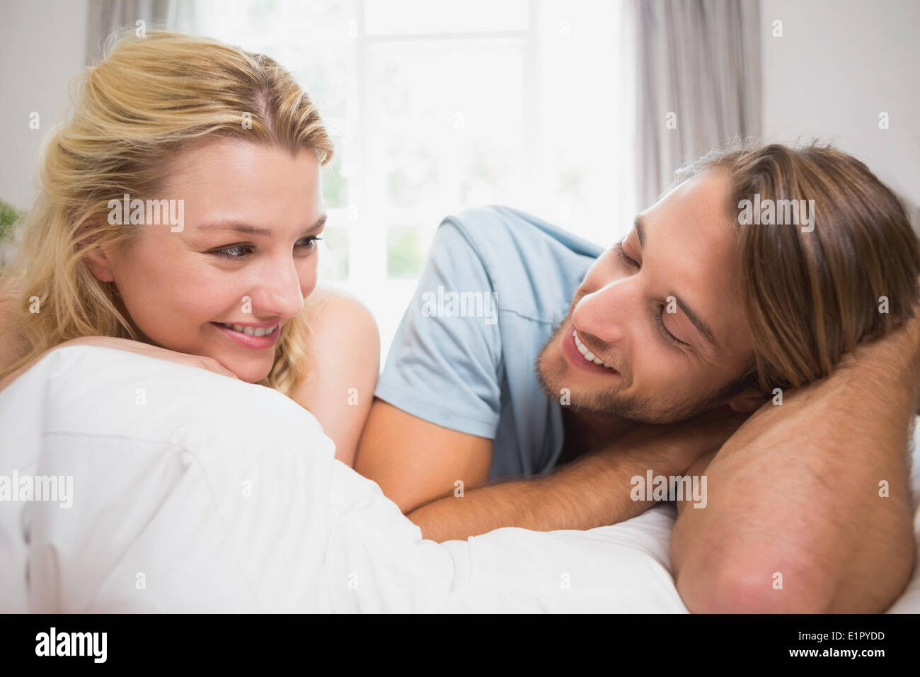 Happy couple relaxing on bed smiling at each other Stock Photo