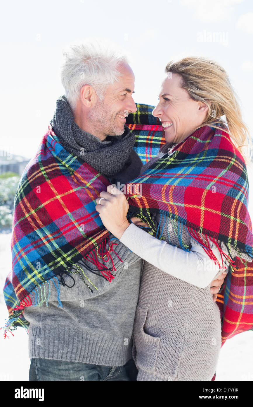 Happy couple wrapped up in blanket standing on the beach Stock Photo