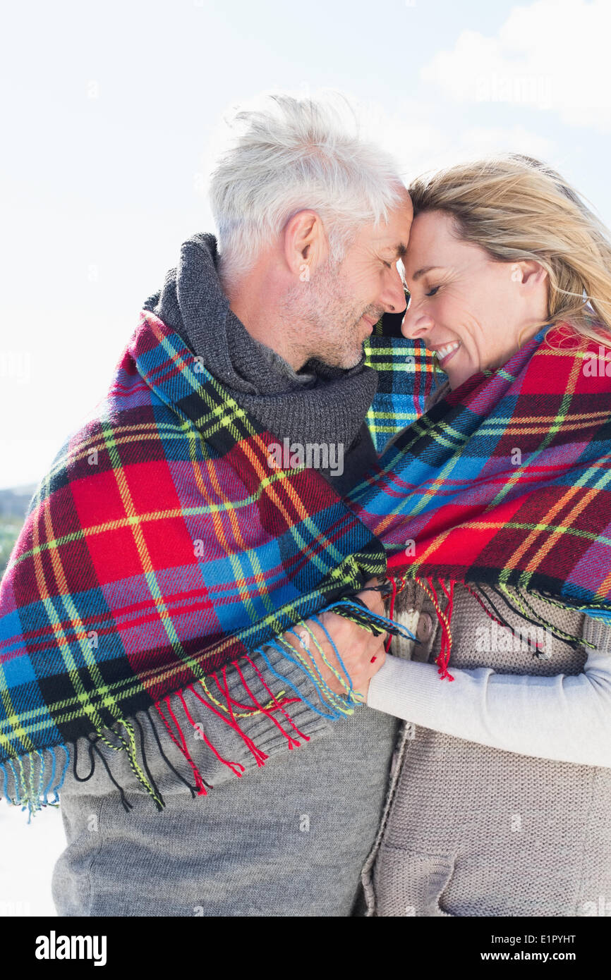 Happy couple wrapped up in blanket standing on the beach Stock Photo