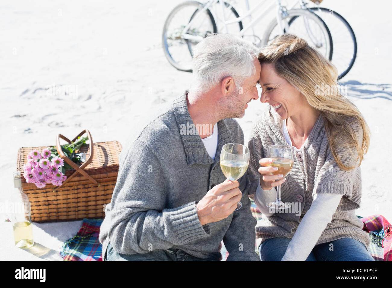 Couple enjoying white wine on picnic at the beach smiling at each other Stock Photo