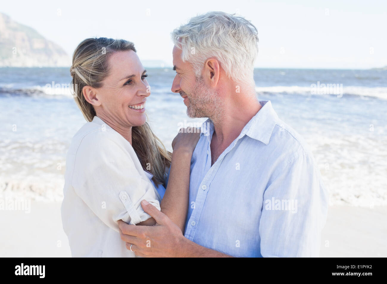 Happy couple hugging on the beach looking at each other Stock Photo