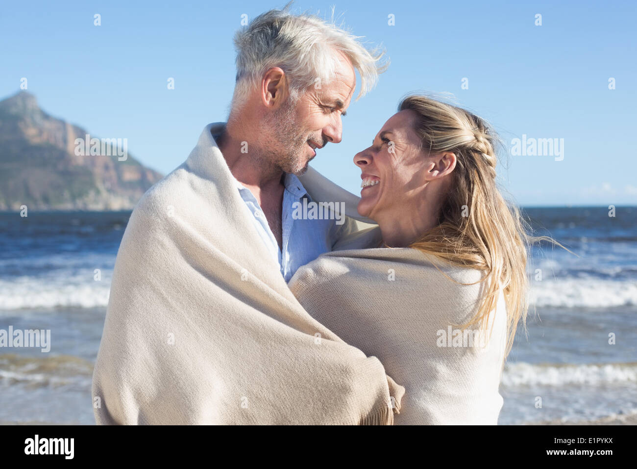 Smiling couple wrapped up in blanket on the beach Stock Photo