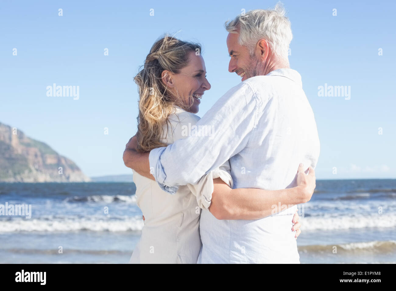Happy couple on the beach smiling at each other Stock Photo