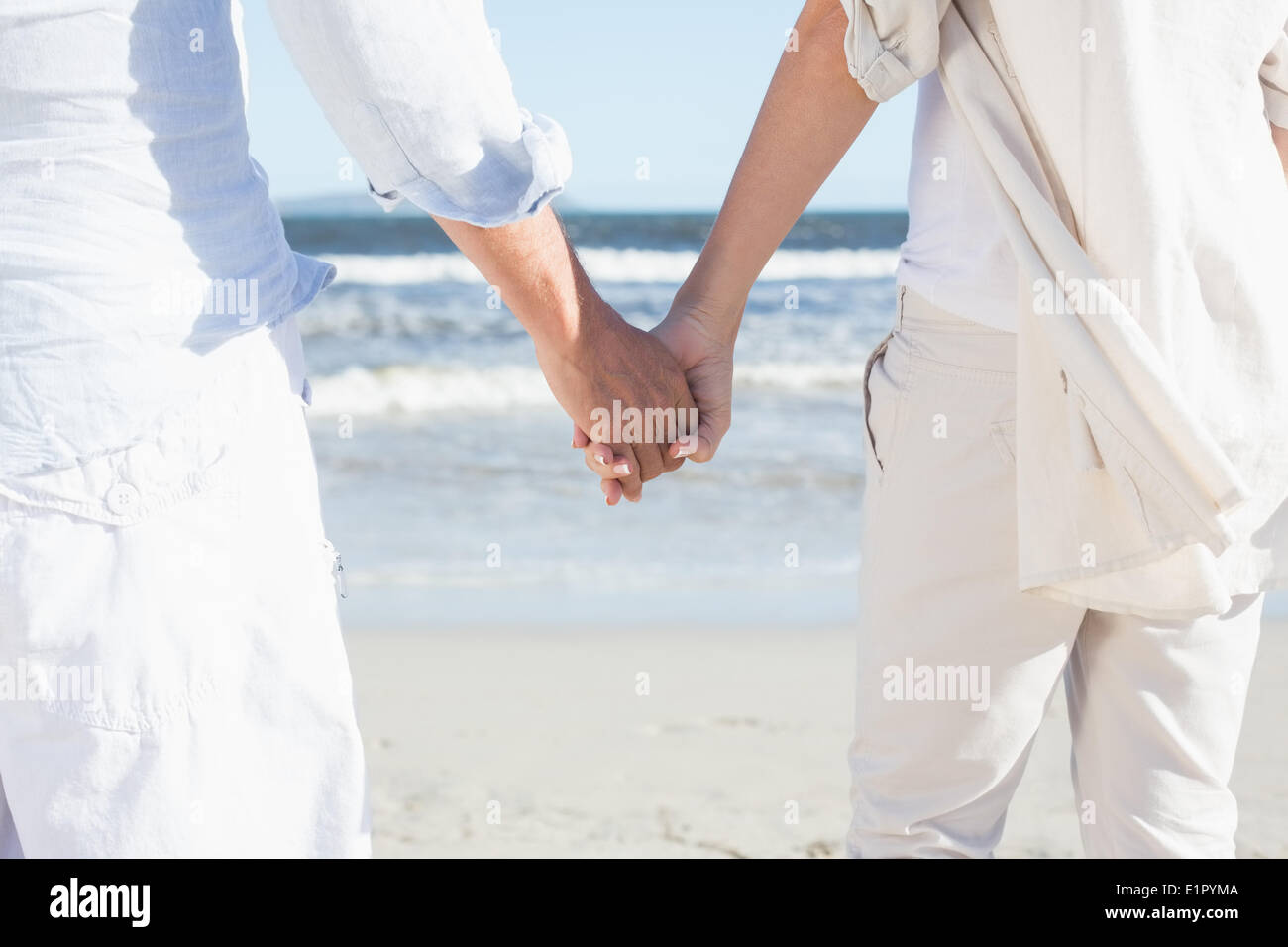 Couple on the beach looking out to sea holding hands Stock Photo - Alamy