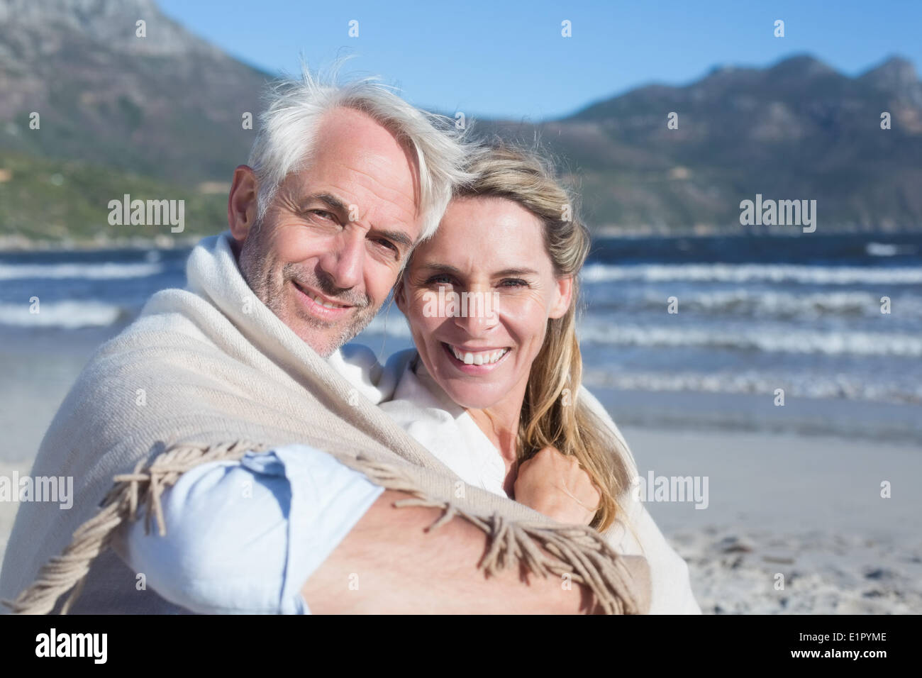 Smiling couple sitting on the beach under blanket Stock Photo - Alamy