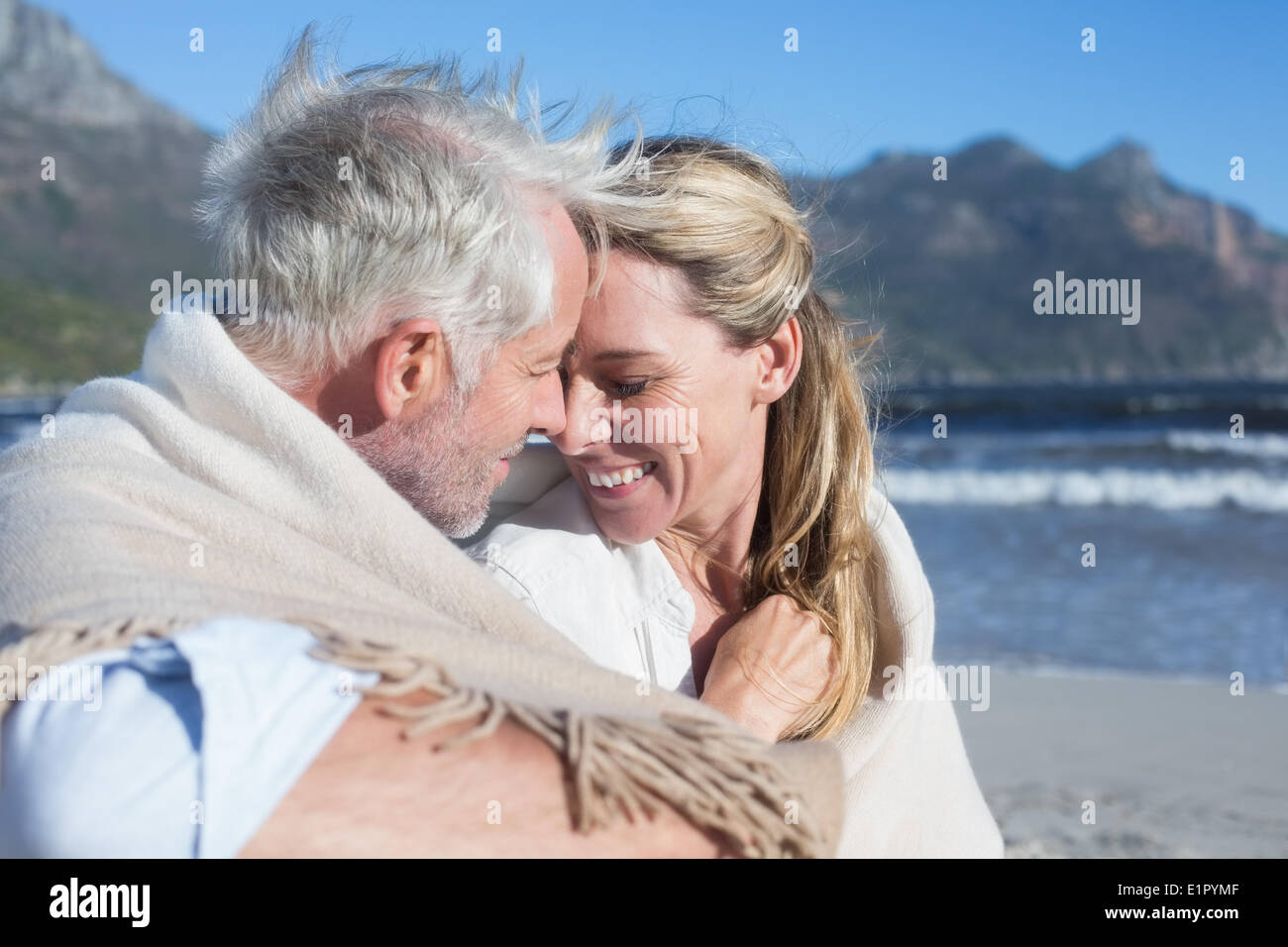 Smiling couple sitting on the beach under blanket Stock Photo