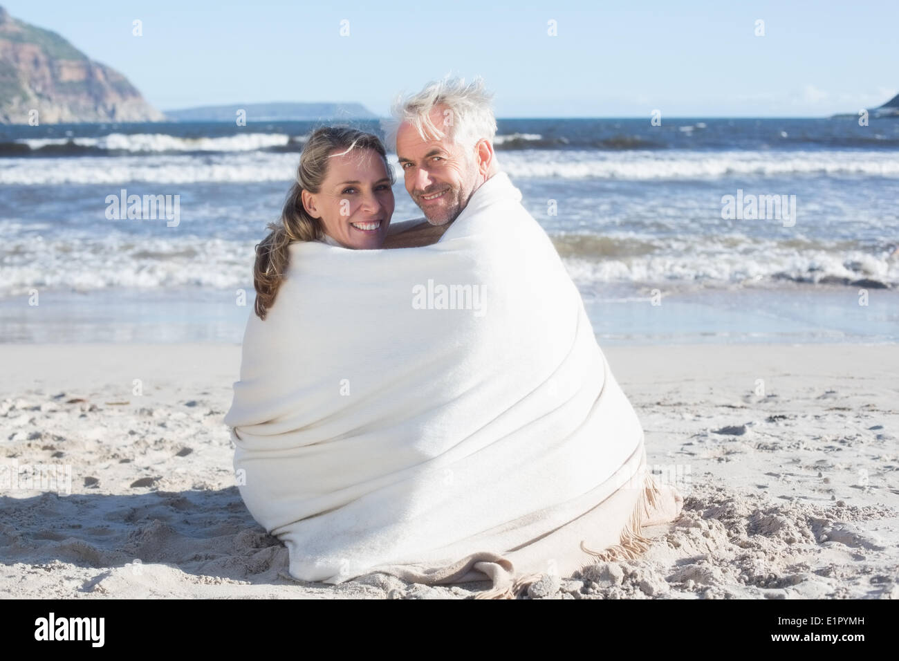 Couple sitting on the beach under blanket smiling at camera Stock Photo ...