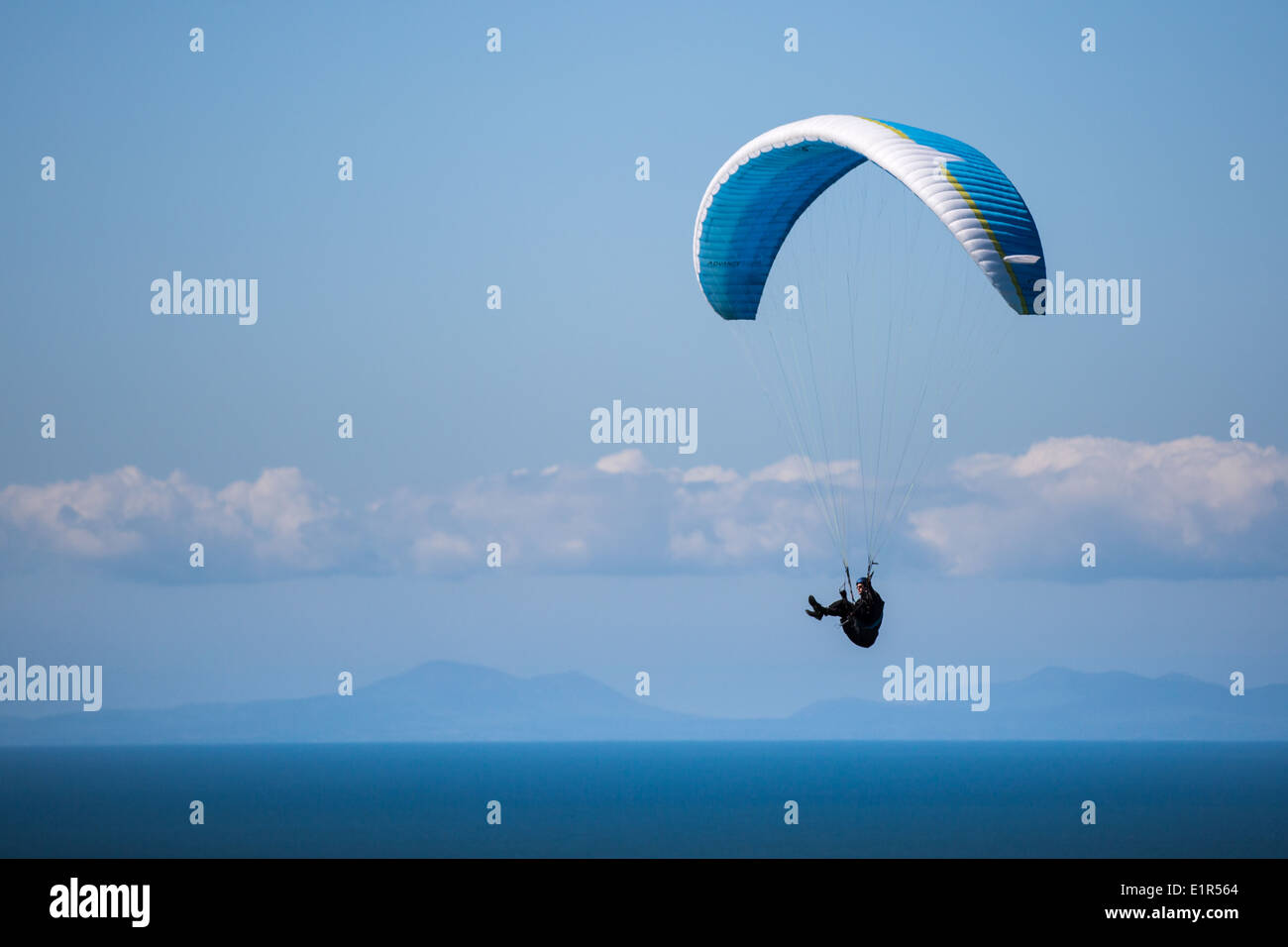 A paraglider over a blue sea with blue sky, clouds and distant mountains. Stock Photo