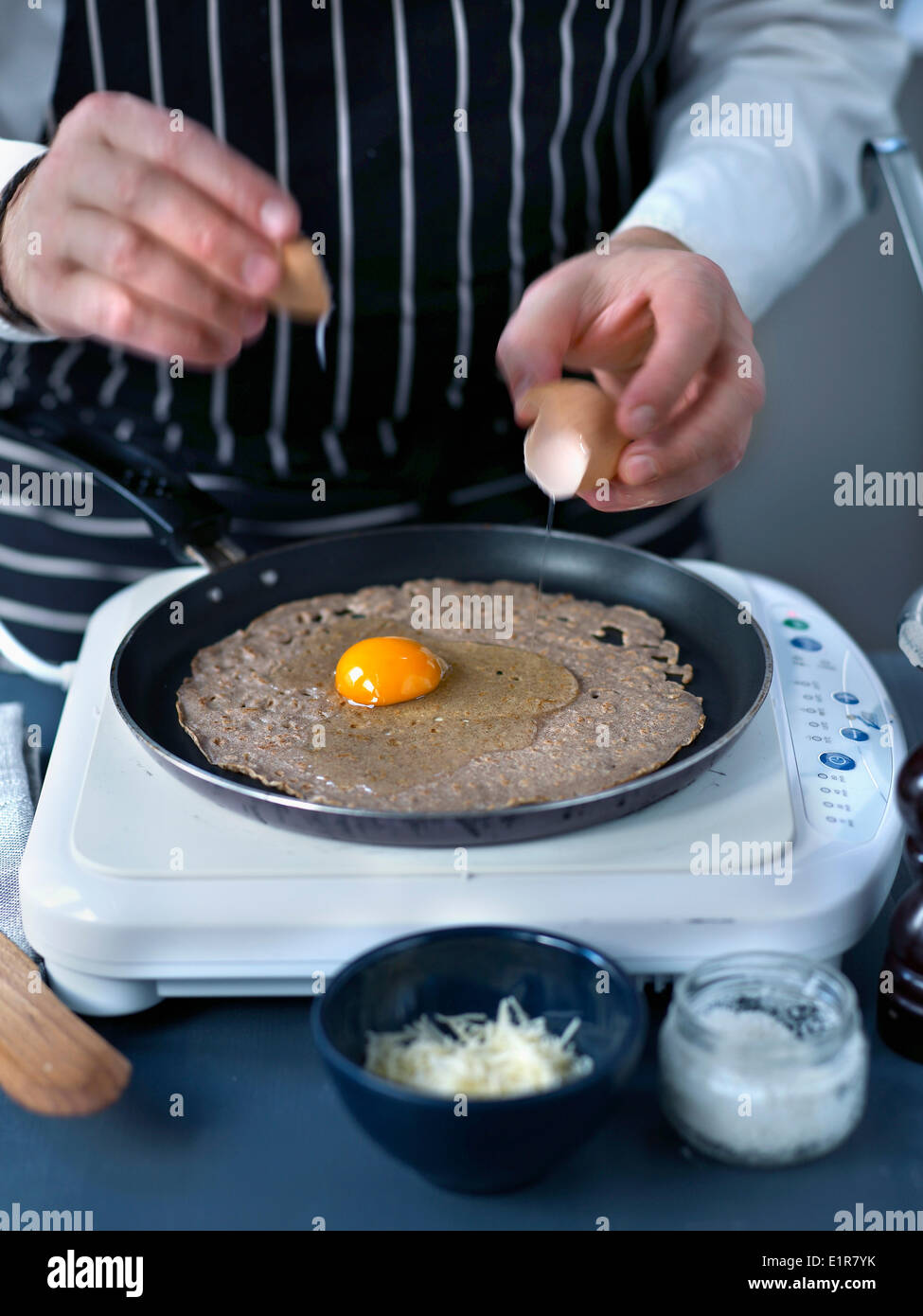 Breaking an egg onto the galette cooking in the frying pan Stock Photo
