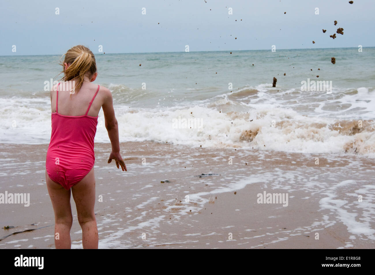young girl throwing sand into the sea Stock Photo
