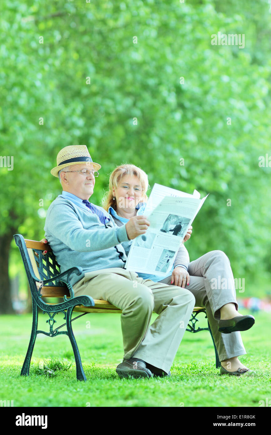 Happy elderly couple sitting in park and reading the news Stock Photo