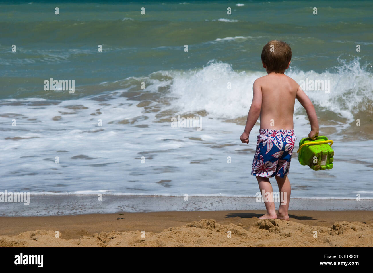 4 year old boy playing at the beach, waiting to catch water in his bucket Stock Photo