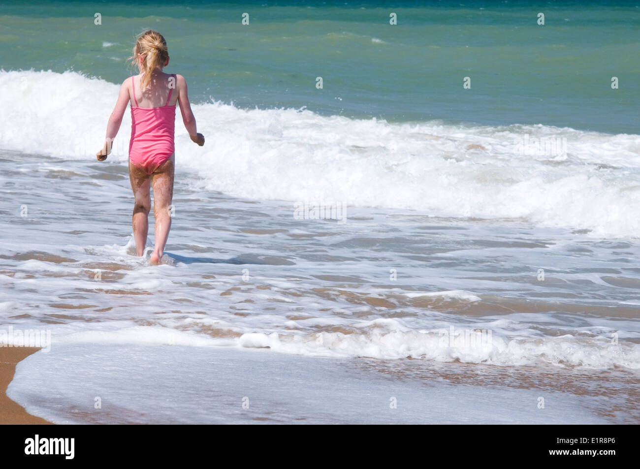 young girl in swimming costume, walking through the surf Stock Photo