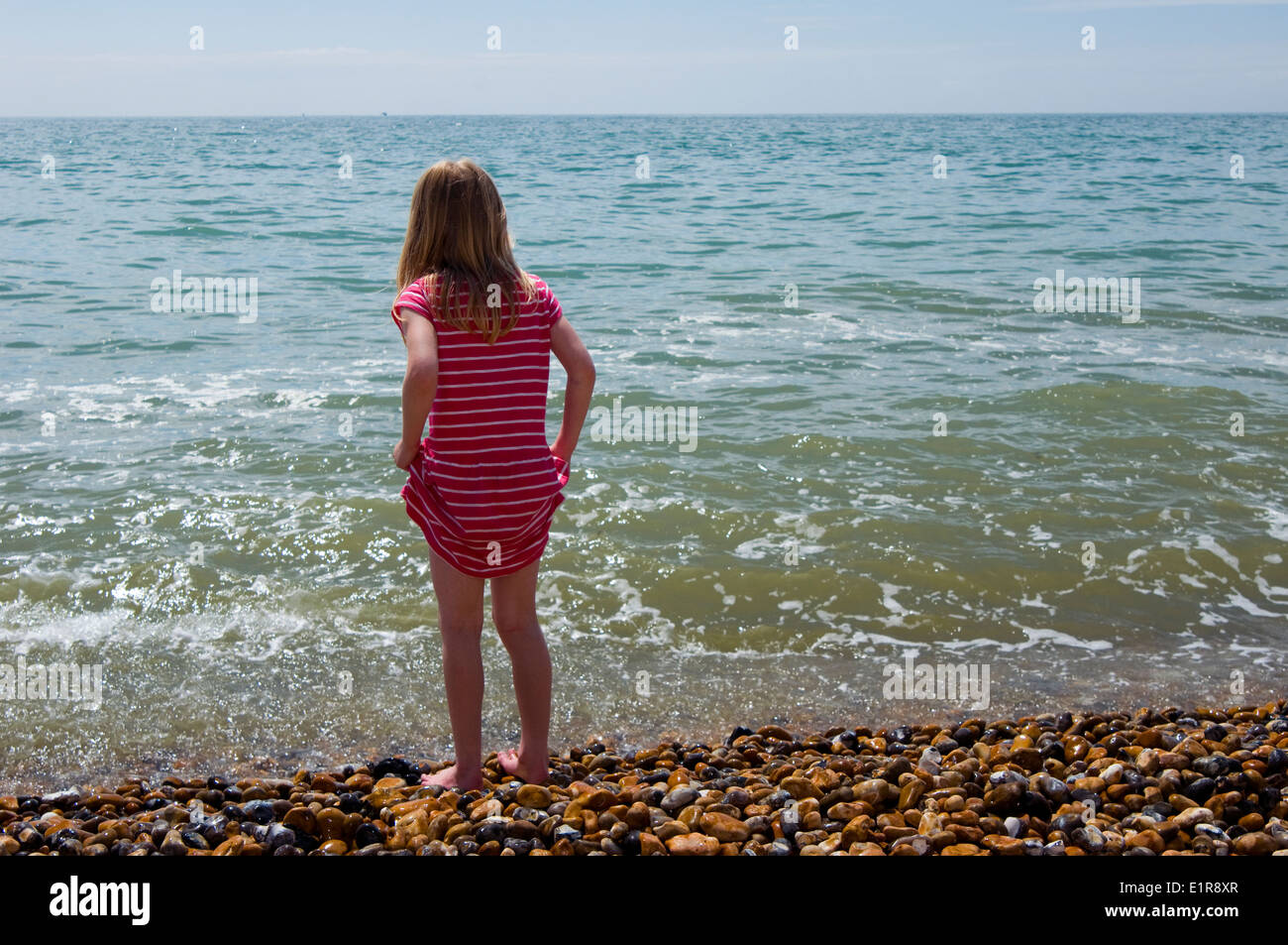 young girl holding up her dress ready to paddle in the sea Stock Photo