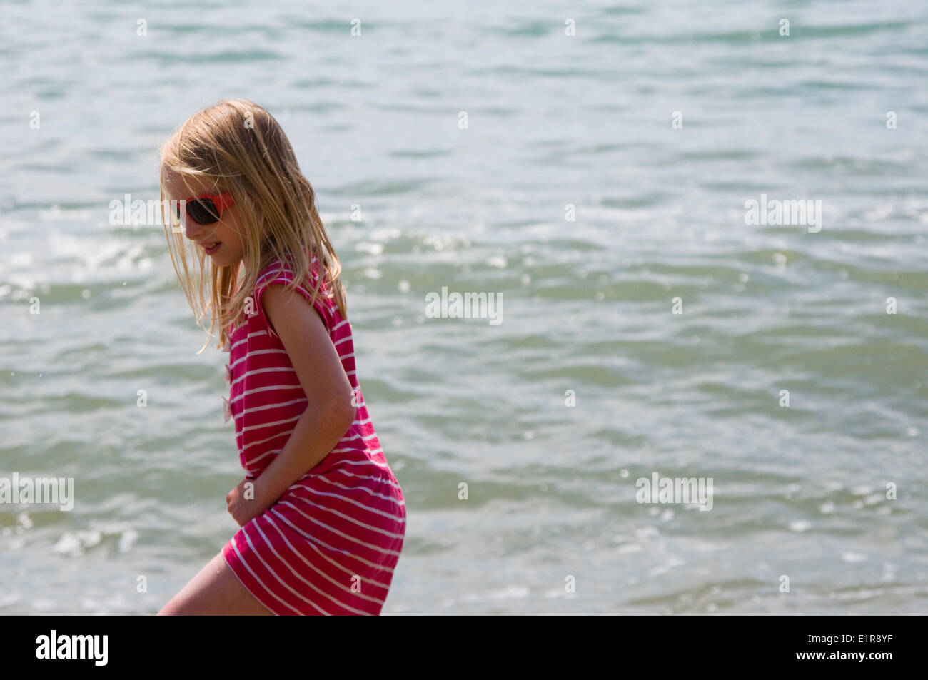 pretty, young blonde girl wearing sunglasses walking by the sea Stock Photo