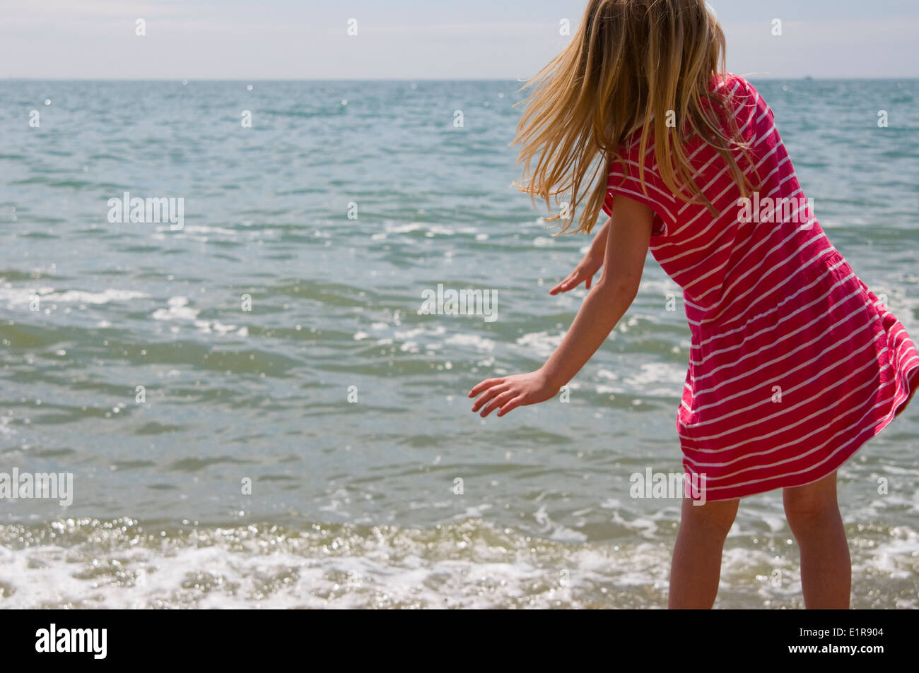 Action shot of young girl who has just thrown a pebble into the sea. Stock Photo