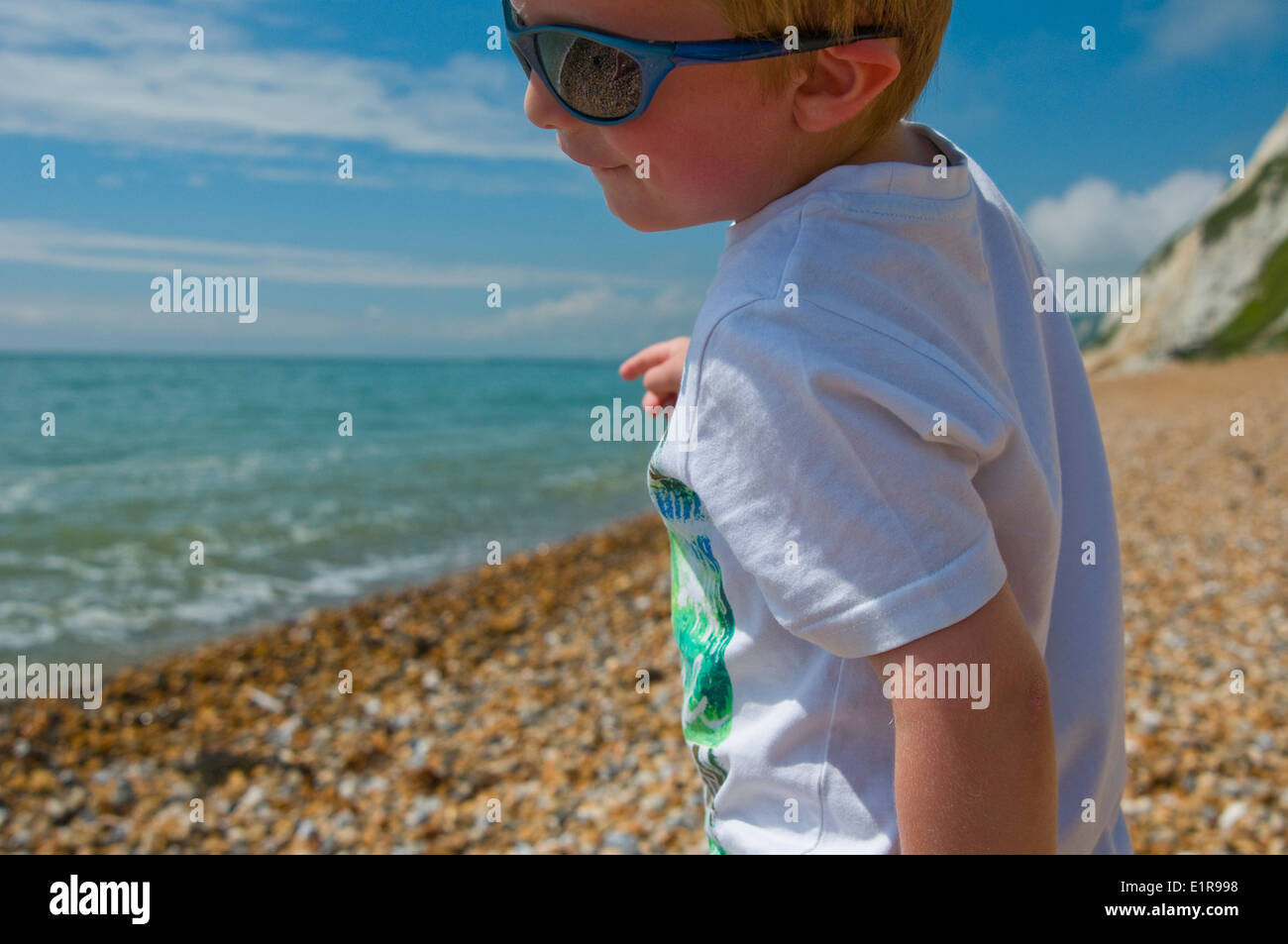 close up of a young boy playing on a pebble beach wearing sunglasses Stock Photo