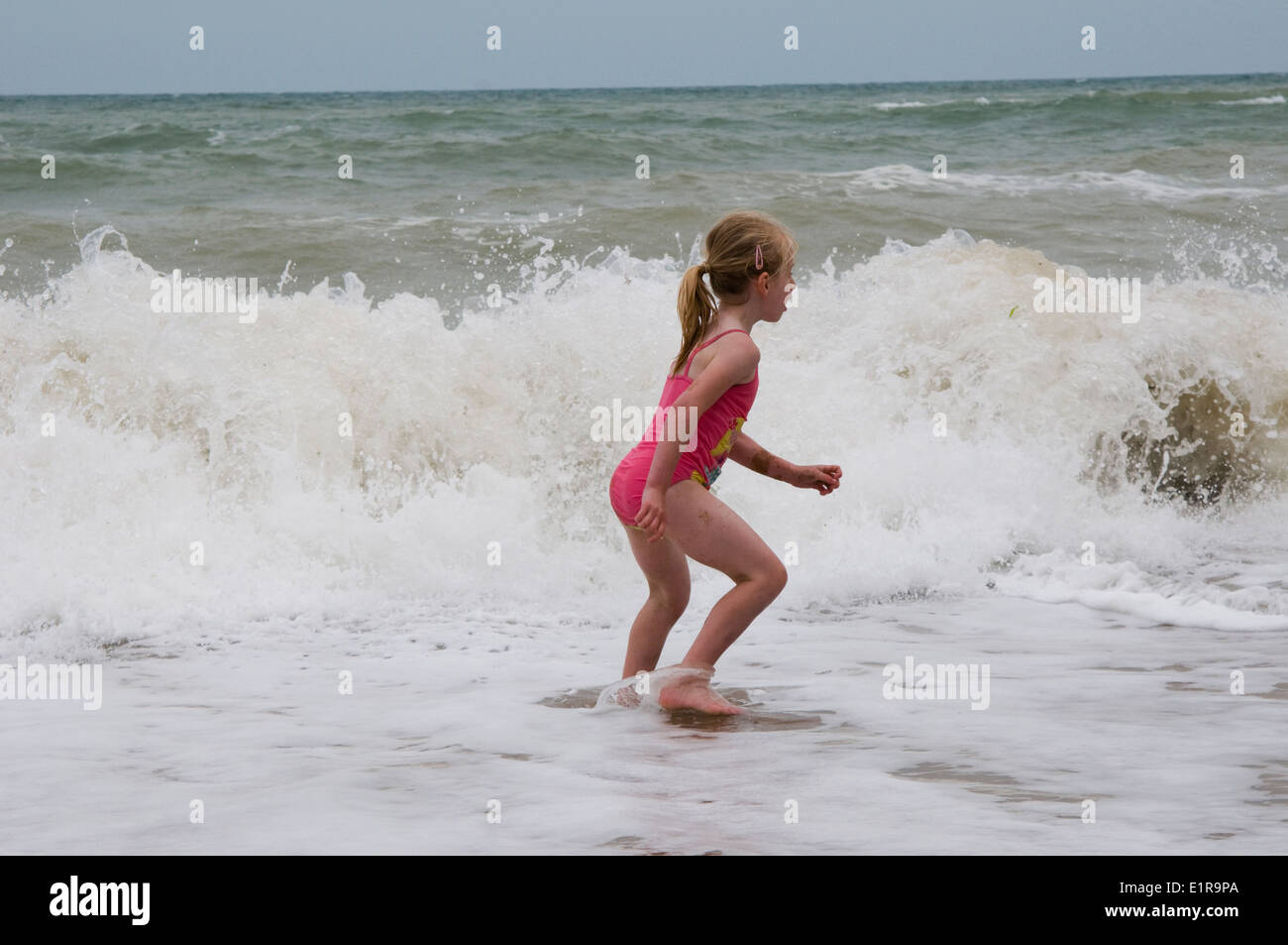 young girl playing in the waves of a rough sea Stock Photo