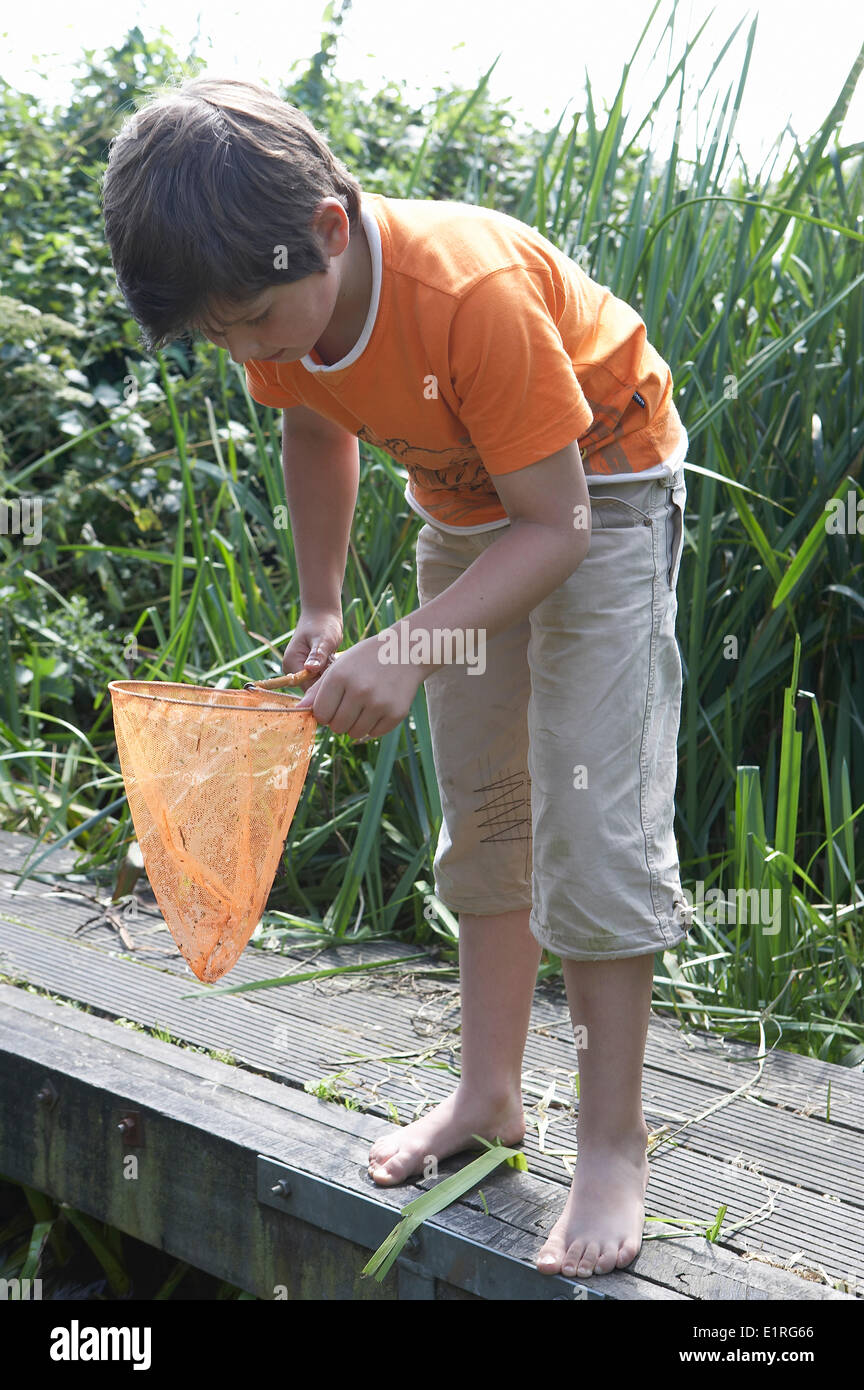 Barefooted young boy on wooden plank wearing orange t-shirt looking into his fishing net Stock Photo