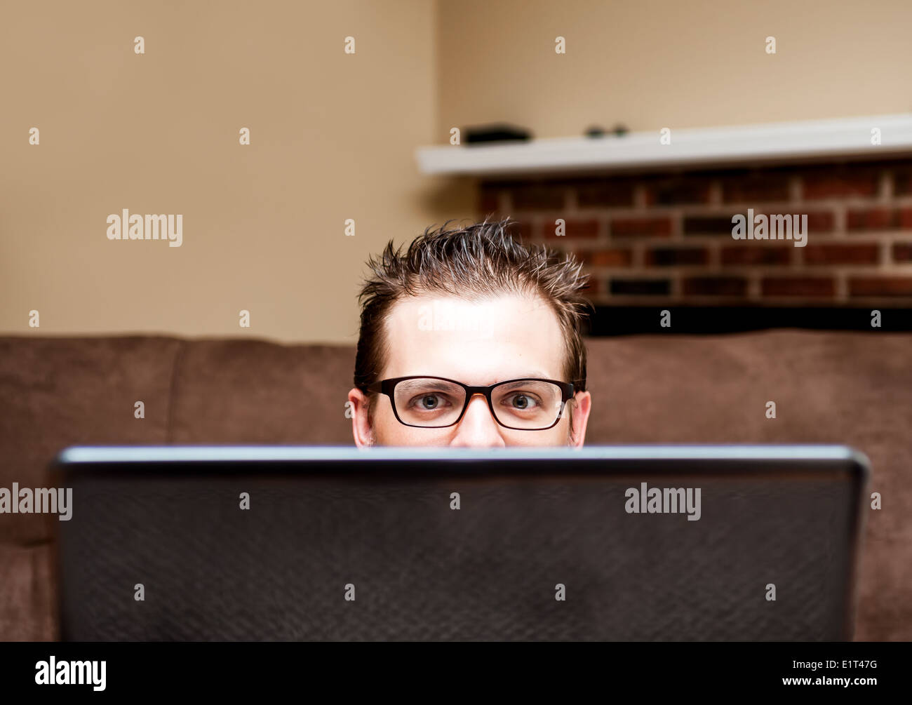 Half-face of European man with glasses hiding behind the laptop Stock Photo