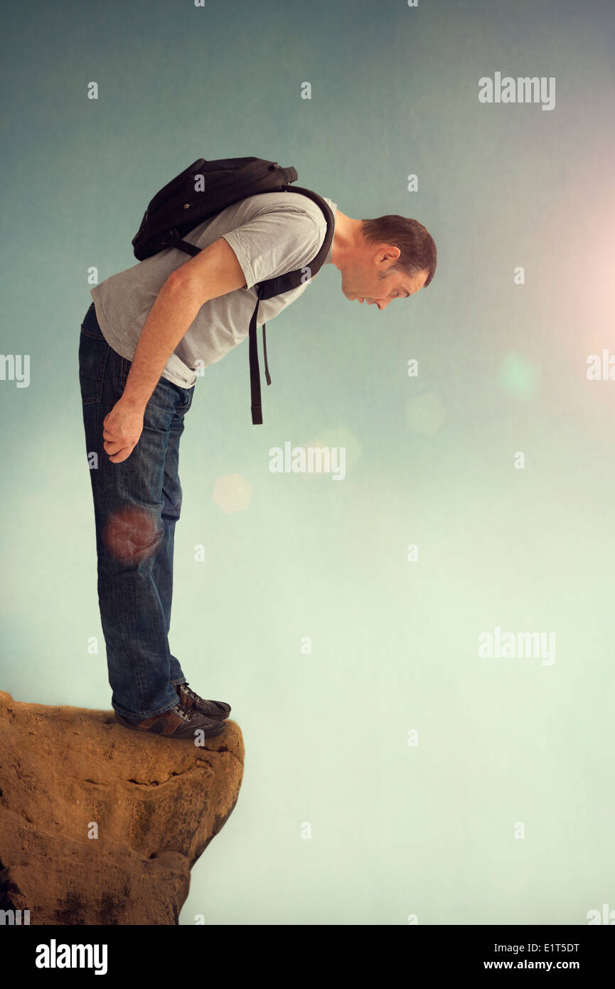 man looking down from a vantage point on a rocky ledge with backpack Stock Photo