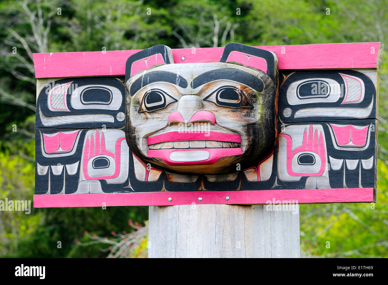 A weathered rectangular bear faced totem with thunderbirds on each side at a burial ground in Alert Bay on Cormorant Island Stock Photo