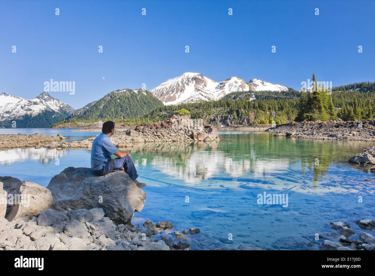Hiker looking at a mountain reflection on Garibaldi Lake, Garibaldi Provincial Park near Whistler in British Columbia, Canada. Stock Photo