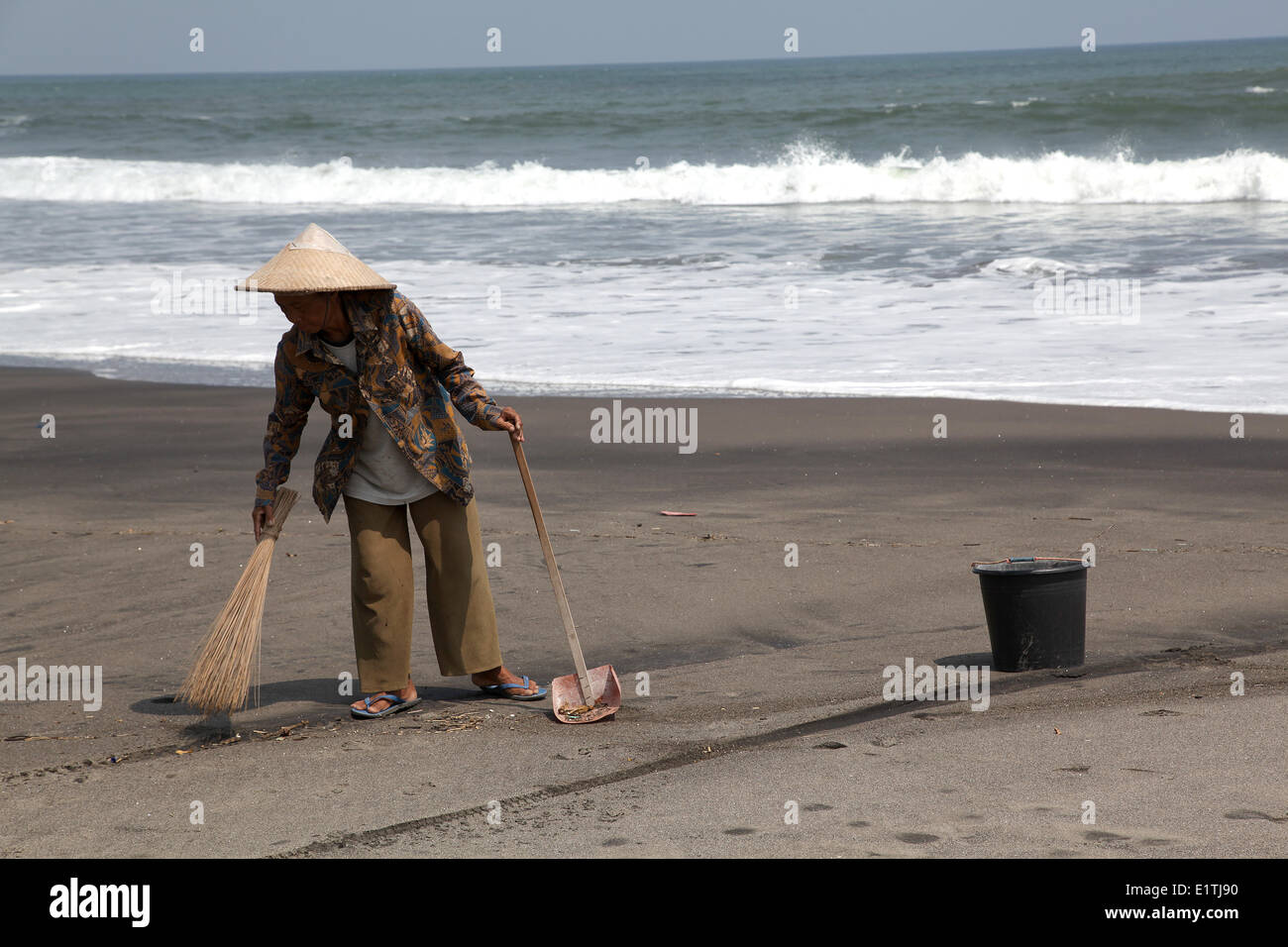 A woman is sweeping a bit of beach in front of a farmer's villa. Few meters further there is just a long beach with no one at. Bali, Indonesia, May 2, 2014. (CTK Photo/Karel Picha) Stock Photo