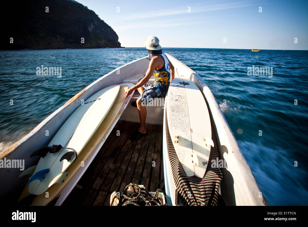 A male surfer catching a boat ride to find the surf. San Juan del Sur, Nicaragua Stock Photo