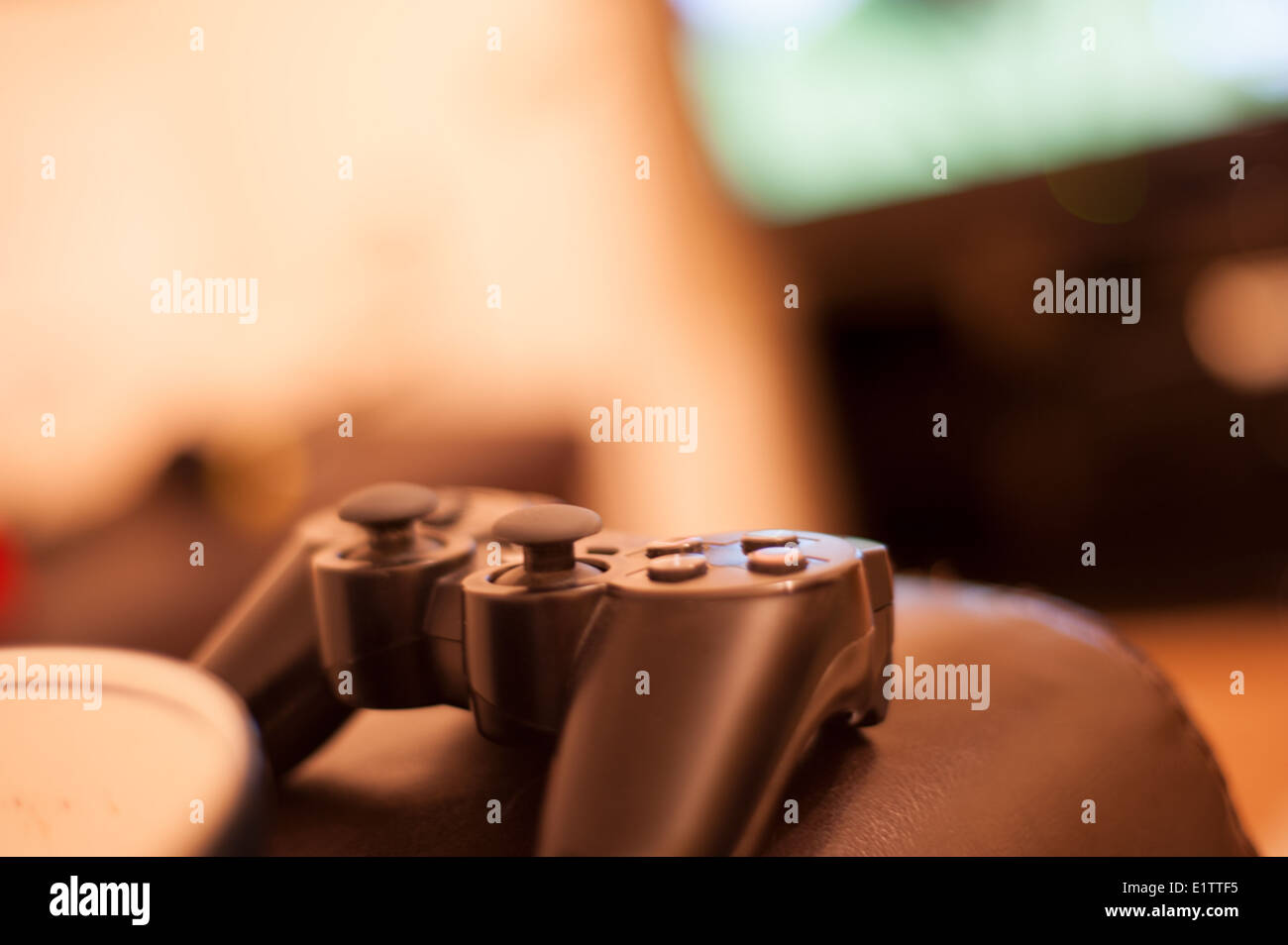 games controller sitting on a sofa arm with football game playing in background Stock Photo