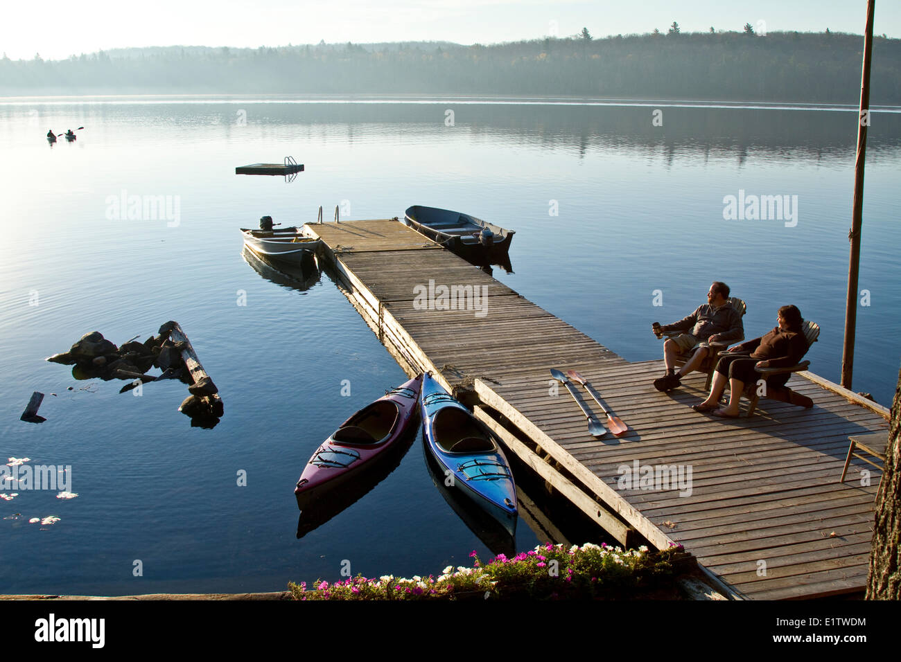 Middle-aged couple enjoy quiet morning on dock near their cottage while thier children kayak on Source Lake Algonquin Park Stock Photo