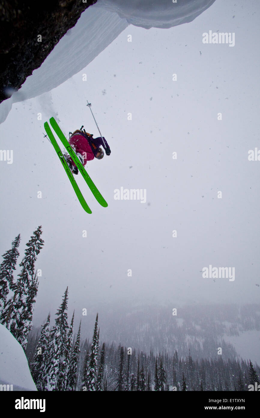 A female backcountry skier drops a cliff on a stormy day. Sol Mountain, Monashee Backcountry, Revelstoke, BC Stock Photo