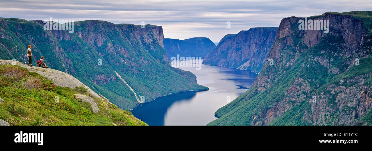 Panorama photo of two hikers enjoying the breathtaking overlooking view of the stunning Western Brook Pond landscape in Gros Mor Stock Photo