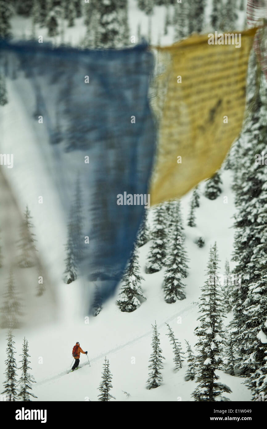 A man ski touring through prayer flags at Icefall Lodge, Canadian Rockies, Golden, BC Stock Photo